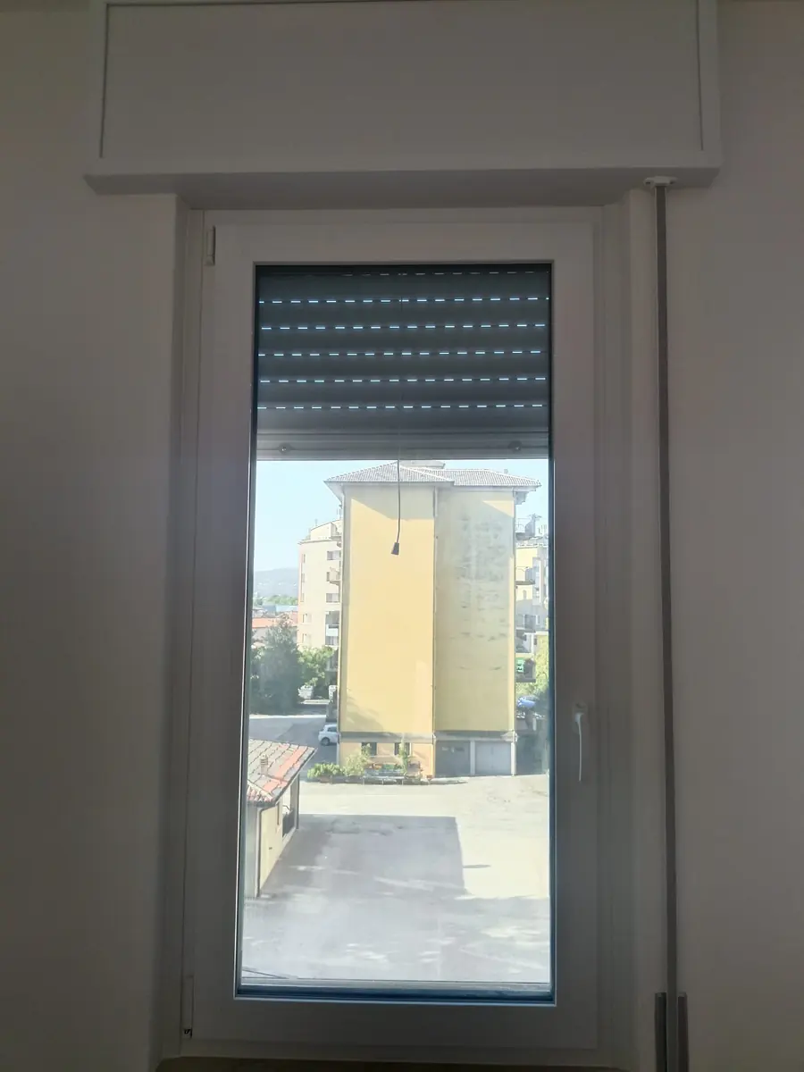Finestra in PVC bianca con tapparella, vista sui tetti